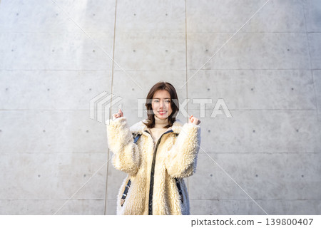 一位年輕女子在水泥牆前擺出勝利的姿勢。 一位年輕女子在水泥牆前擺出勝利的姿勢。 139800407