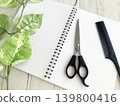 Hairdressing studies and training courses; an open ring notebook and hair-cutting scissors; a hair salon idea book and diary; houseplants and a comb. 139800416