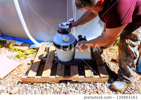 Service man is connecting pool filter to pool in his backyard during bright weather. Service man is connecting pool filter to pool in his backyard during bright weather. 139803161
