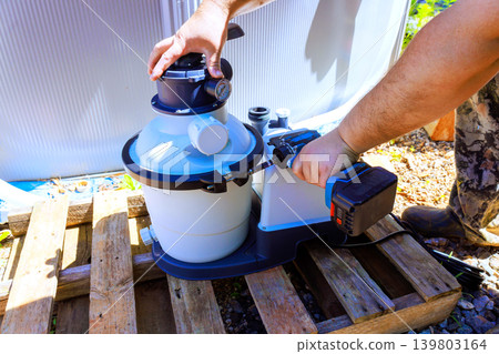 Worker works on setting up pool filter in backyard on sunny day while using power tools Worker works on setting up pool filter in backyard on sunny day while using power tools 139803164