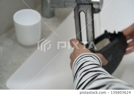 A woman cleaning the dustbin of a robot vacuum cleaner. A woman cleaning the dustbin of a robot vacuum cleaner. 139803624