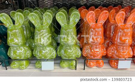 Bright green and orange glossy ceramic bunny figurines standing in neat rows on a retail store shelf Bright green and orange glossy ceramic bunny figurines standing in neat rows on a retail store shelf 139803723
