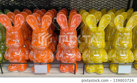Bright orange and yellow glossy ceramic bunny figurines standing in rows on a modern retail shelf 139803724