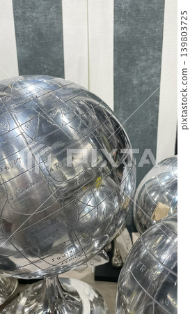 Chic modern silver metal globe with engraved world map details displayed against a striped background Chic modern silver metal globe with engraved world map details displayed against a striped background 139803725