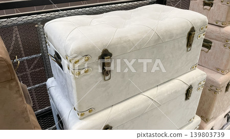 Elegant white velvet tufted storage trunks with brass hardware stacked in a chic modern interior Elegant white velvet tufted storage trunks with brass hardware stacked in a chic modern interior 139803739