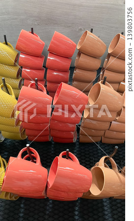 Neat retail display of colorful ceramic coffee mugs in orange yellow and beige shades stacked on hooks in a store Neat retail display of colorful ceramic coffee mugs in orange yellow and beige shades stacked on hooks in a store 139803756