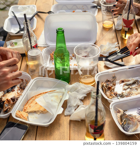 Used takeaway food containers, empty bottles, leftovers are scattered on wooden table after an outdoor meal. Concept of waste, pollution, environmental, disposable packaging, single use plastic waste Used takeaway food containers, empty bottles, leftovers are scattered on wooden table after an outdoor meal. Concept of waste, pollution, environmental, disposable packaging, single use plastic waste 139804159
