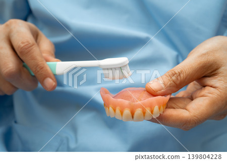 Asian senior woman patient clean teeth denture with toothbrush for chew food. Asian senior woman patient clean teeth denture with toothbrush for chew food. 139804228