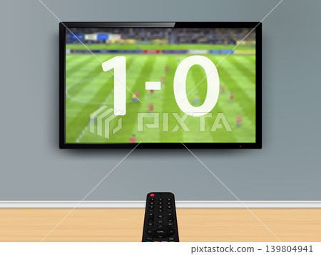 Watching online soccer match. Remote control is pointed at the TV on the wall with live soccer match result on screen. 139804941