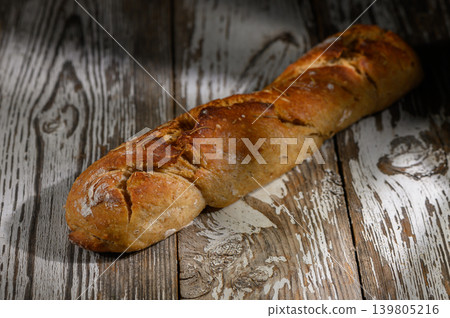 Rustic loaf of artisan bread resting on weathered wooden table in soft lighting Rustic loaf of artisan bread resting on weathered wooden table in soft lighting 139805216