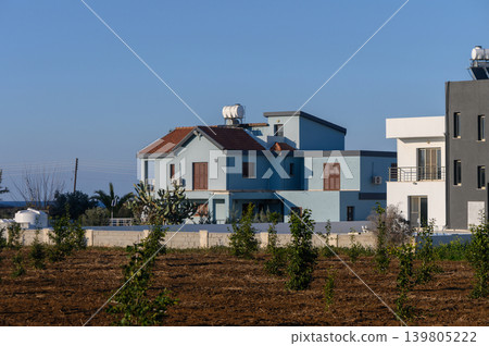 Blue villa surrounded by young trees under a clear sky in a tranquil countryside setting Blue villa surrounded by young trees under a clear sky in a tranquil countryside setting 139805222