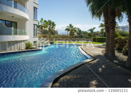 Tranquil oasis with a swimming pool surrounded by palm trees on a sunny day. Tranquil oasis with a swimming pool surrounded by palm trees on a sunny day. 139805231