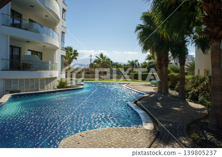 Serene tropical getaway featuring a shimmering pool surrounded by lush palm trees on a sunny day. Serene tropical getaway featuring a shimmering pool surrounded by lush palm trees on a sunny day. 139805237