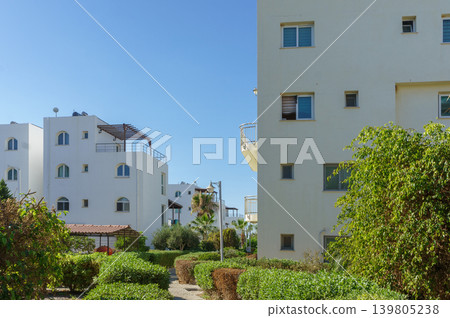 Bright white buildings surrounded by lush greenery in a sunny neighborhood, evoking a tranquil retreat. Bright white buildings surrounded by lush greenery in a sunny neighborhood, evoking a tranquil retreat. 139805238