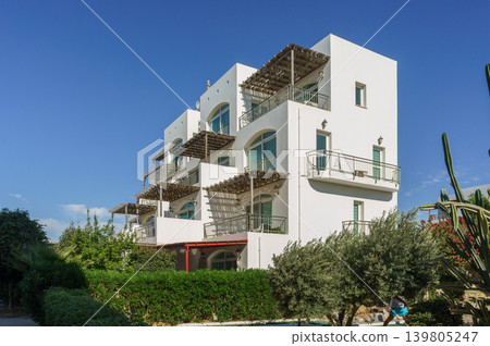 Modern white architecture blends with lush greenery at a vibrant coastal property on a sunny day. 139805247