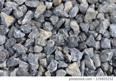 Natural gravel stones in various shades laid out in a textured surface capturing light and shadow in an outdoor setting 139805252