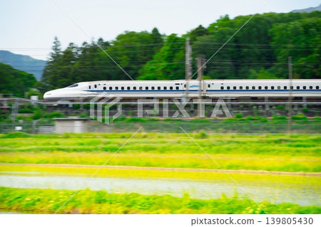 東海道新幹線飛馳穿過鬱鬱蔥蔥的綠地——鏡頭搖攝。 東海道新幹線飛馳穿過鬱鬱蔥蔥的綠地——鏡頭搖攝。 139805430