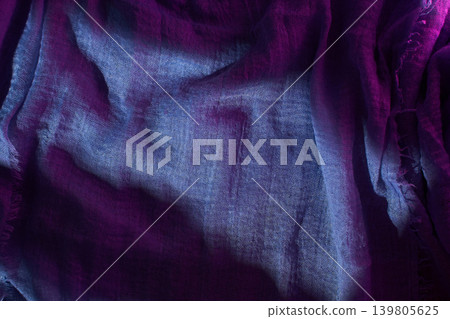 A piece of fabric lies on a surface as light catches its texture. The colors blend from purple to blue A piece of fabric lies on a surface as light catches its texture. The colors blend from purple to blue 139805625