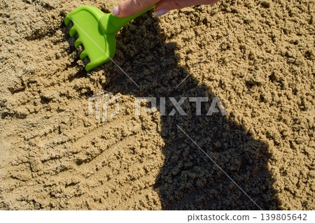 Detailed shot of a plastic toy rake smoothing out damp sandy soil 139805642