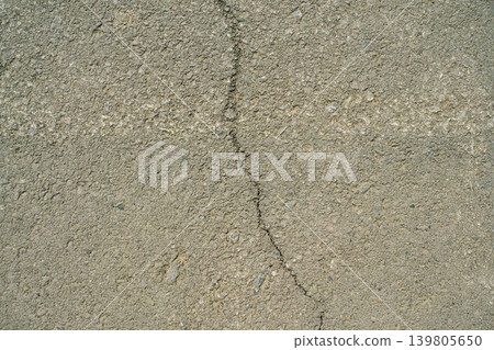 A top-down close-up shot of an uneven grey asphalt surface featuring a continuous vertical narrow crack A top-down close-up shot of an uneven grey asphalt surface featuring a continuous vertical narrow crack 139805650