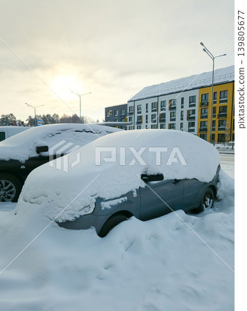 Snow covers the roofs and windshields of parked cars in a residential area. The sun sets in the background Snow covers the roofs and windshields of parked cars in a residential area. The sun sets in the background 139805677