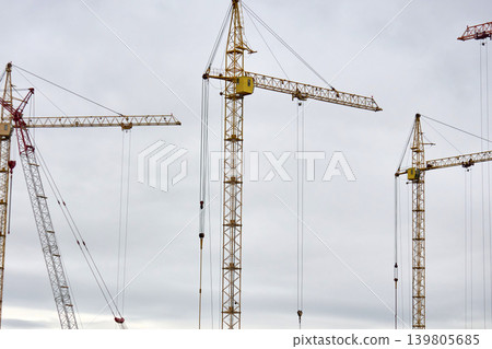 Crane operation above incomplete structure under cloudy sky. Urban development scene showing cranes and concrete core against overcast sky mood Crane operation above incomplete structure under cloudy sky. Urban development scene showing cranes and concrete core against overcast sky mood 139805685