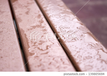 Raindrops collect on the surface of a wooden bench in a city park Raindrops collect on the surface of a wooden bench in a city park 139805694