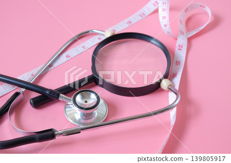 A magnifying glass with measuring tape and stethoscope. A magnifying glass with measuring tape and stethoscope. 139805917