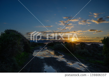 Golden sunset illuminates muddy path through lush landscape in serene evening light Golden sunset illuminates muddy path through lush landscape in serene evening light 139806337