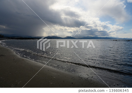Glistening waves lap against the shore beneath a dramatic sky reflecting on tranquil waters Glistening waves lap against the shore beneath a dramatic sky reflecting on tranquil waters 139806345