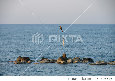Lonely streetlight standing guard over calm ocean waves at dusk Lonely streetlight standing guard over calm ocean waves at dusk 139806346