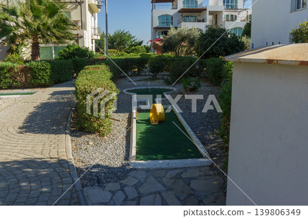 A charming miniature golf course nestled in a tranquil garden setting on a sunny day. A charming miniature golf course nestled in a tranquil garden setting on a sunny day. 139806349