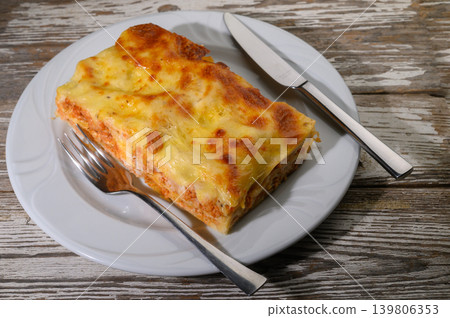 Deliciously baked lasagna resting on a rustic wooden table, perfectly prepared and ready to be enjoyed at a cozy Italian restaurant Deliciously baked lasagna resting on a rustic wooden table, perfectly prepared and ready to be enjoyed at a cozy Italian restaurant 139806353