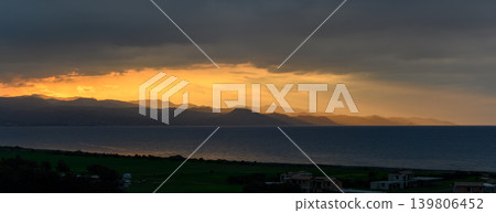 Golden sunset over distant mountains reflecting on calm waters of the coastline Golden sunset over distant mountains reflecting on calm waters of the coastline 139806452