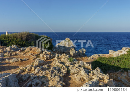 Tranquil coastal landscape with rocky shoreline and deep blue sea during a clear sunny day. 139806584