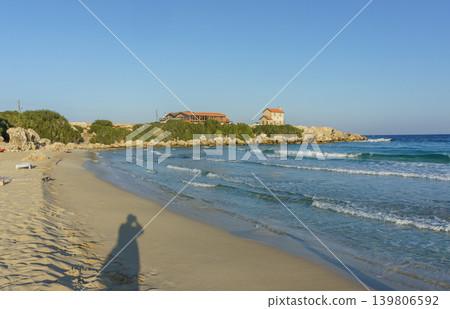 A tranquil beach landscape at sunset with gentle waves and distant buildings in the background. A tranquil beach landscape at sunset with gentle waves and distant buildings in the background. 139806592