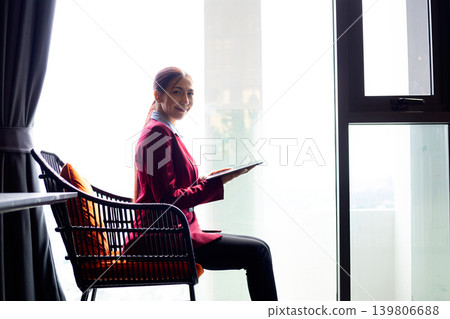 Confident businesswoman holding digital tablet while sitting near large office window, professional female executive working in modern workspace with natural light and corporate lifestyle concept Confident businesswoman holding digital tablet while sitting near large office window, professional female executive working in modern workspace with natural light and corporate lifestyle concept 139806688