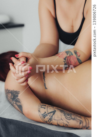 Woman relaxes with hands clasped, tattoos visible on arms Woman relaxes with hands clasped, tattoos visible on arms 139806726