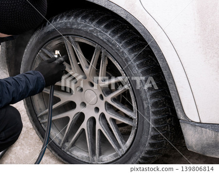 Man inflating dirty car tire. Driver checks air pressure. Auto service maintenance, transportation safety, road trip concept. 139806814
