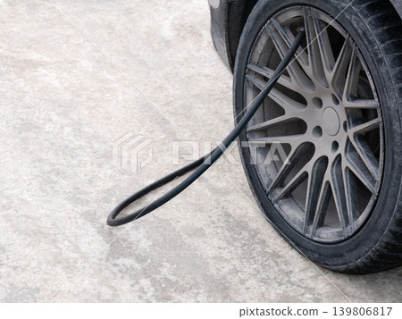 Tire inflator hose connected to a dirty car wheel on a concrete ground. Concept of flat tire, car repair, and vehicle maintenance. 139806817
