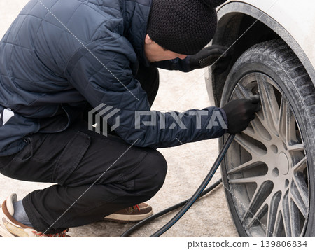 Man filling air in car tire with pump hose. Vehicle maintenance and safety. Automotive care and roadside assistance concept. Man filling air in car tire with pump hose. Vehicle maintenance and safety. Automotive care and roadside assistance concept. 139806834