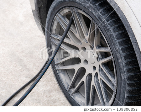 Dirty car wheel with air hose attached. Checking and inflating tire for safe driving and maintenance. Automotive service concept. Dirty car wheel with air hose attached. Checking and inflating tire for safe driving and maintenance. Automotive service concept. 139806852