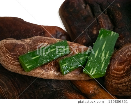 Fresh aloe vera pieces with water drops lie on dark driftwood on white background. Natural organic cosmetic ingredient for skincare. Fresh aloe vera pieces with water drops lie on dark driftwood on white background. Natural organic cosmetic ingredient for skincare. 139806861