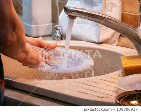Woman washing dish under running water in kitchen sink. Doing household chores and daily routine concept. Cleaning and hygiene habit. 139806917