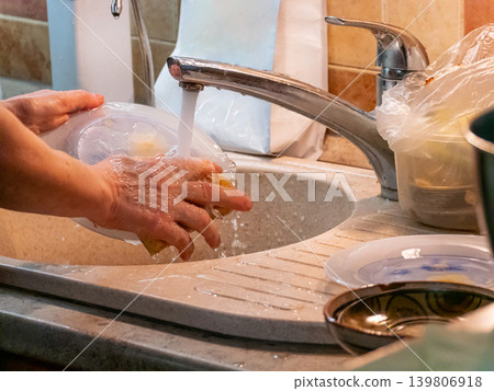 Woman washing dish in kitchen sink, household chore. Daily routine for home, hygiene maintenance. Cleanliness and domestic life. Woman washing dish in kitchen sink, household chore. Daily routine for home, hygiene maintenance. Cleanliness and domestic life. 139806918