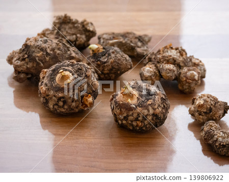 Several fresh taro roots with small sprouts on a light brown wooden surface. Food ingredient traditional asian cooking. Several fresh taro roots with small sprouts on a light brown wooden surface. Food ingredient traditional asian cooking. 139806922