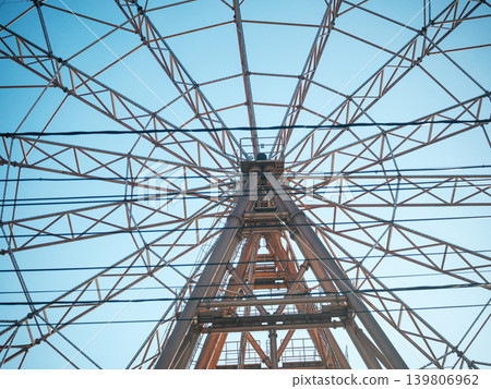 Ferris wheel frame viewed from below. Abstract geometric pattern of metal beams against a clear blue sky. Amusement park architecture structure. 139806962