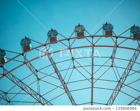 Part of a ferris wheel structure with cabins against a clear blue sky. Amusement park attraction for entertainment and recreation. Part of a ferris wheel structure with cabins against a clear blue sky. Amusement park attraction for entertainment and recreation. 139806966