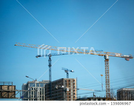 Construction site with several tower cranes against a clear blue sky, showing ongoing building work and urban development. 139806967