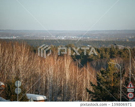 Winter forest landscape with bare birch trees and distant village. Natural woodland scenery for travel and outdoor concept. Winter forest landscape with bare birch trees and distant village. Natural woodland scenery for travel and outdoor concept. 139806971